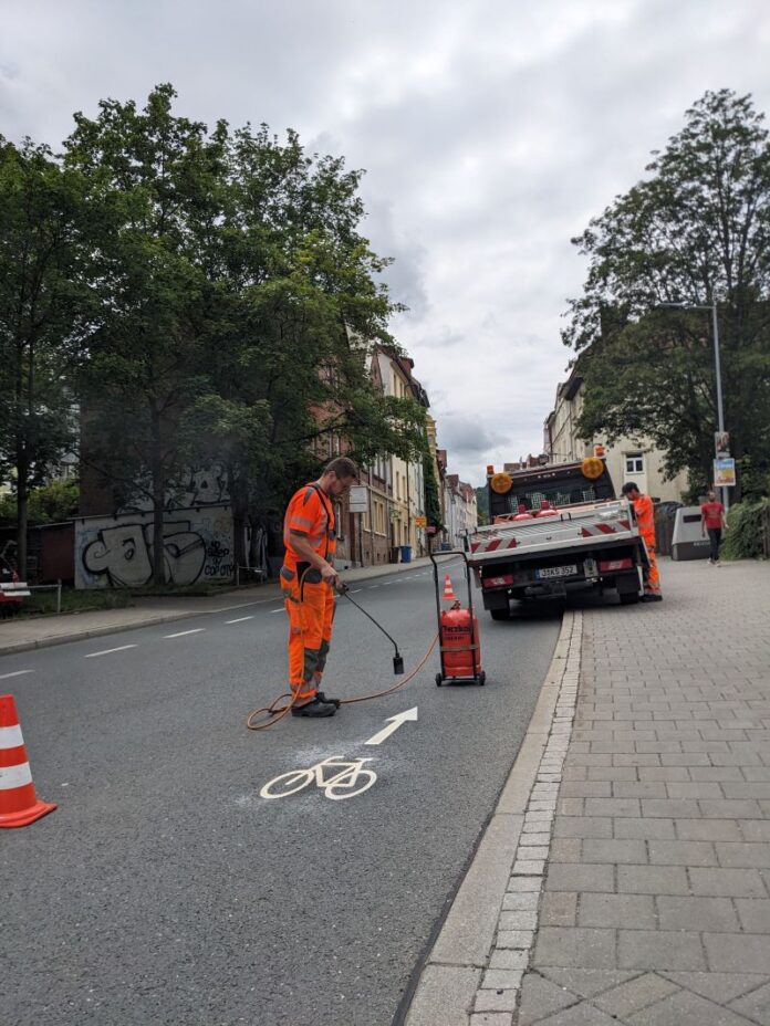 Ein Mitarbeiter vom Kommunalservice Jena bringt auf dem Magdelstieg ein Fahrrad-Piktogramm auf die Straße auf.